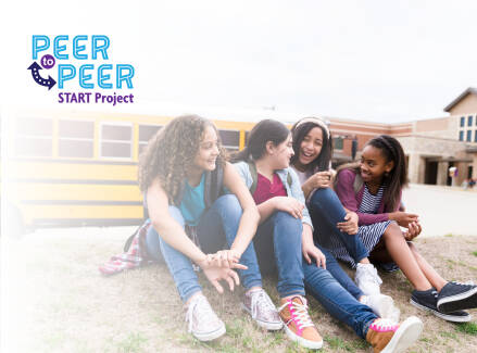 Four teens sitting in front of a school bus